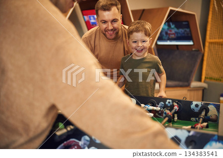 Playing table football game indoors. Family of dad, mother and son that are indoors 134383541