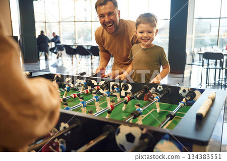 Smiling, enjoying. Family of dad, mother and son that are playing table football game indoors 134383551