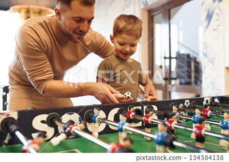 Teaching how to play. Father and son are playing table football game indoors Teaching how to play. Father and son are playing table football game indoors 134384138
