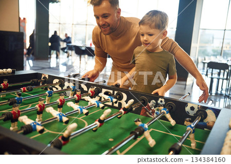 Conception of entertainment. Father and son are playing table football game indoors Conception of entertainment. Father and son are playing table football game indoors 134384160