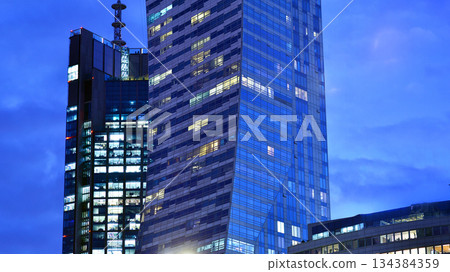Office building in the evening with lightened workspaces. Modern, glazed skyscraper in financial district. Late hours in the office. Office building in the evening with lightened workspaces. Modern, glazed skyscraper in financial district. Late hours in the office. 134384359