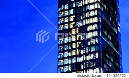 Office building in the evening with lightened workspaces. Modern, glazed skyscraper in financial district. Late hours in the office. Office building in the evening with lightened workspaces. Modern, glazed skyscraper in financial district. Late hours in the office. 134384362