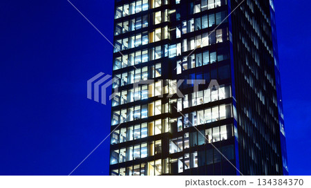 Office building in the evening with lightened workspaces. Modern, glazed skyscraper in financial district. Late hours in the office. Office building in the evening with lightened workspaces. Modern, glazed skyscraper in financial district. Late hours in the office. 134384370