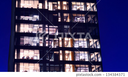 Office building in the evening with lightened workspaces. Modern, glazed skyscraper in financial district. Late hours in the office. Office building in the evening with lightened workspaces. Modern, glazed skyscraper in financial district. Late hours in the office. 134384371