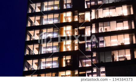 Office building in the evening with lightened workspaces. Modern, glazed skyscraper in financial district. Late hours in the office. 134384373