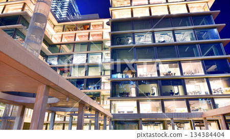 Office building in the evening with lightened workspaces. Modern, glazed skyscraper in financial district. Late hours in the office. Office building in the evening with lightened workspaces. Modern, glazed skyscraper in financial district. Late hours in the office. 134384404