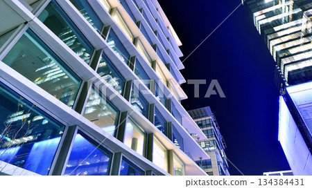 Office building in the evening with lightened workspaces. Modern, glazed skyscraper in financial district. Late hours in the office. Office building in the evening with lightened workspaces. Modern, glazed skyscraper in financial district. Late hours in the office. 134384431