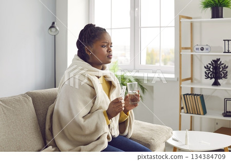 Sick young africanamerican woman feels unwell and is going to drink medicine. Sick young africanamerican woman feels unwell and is going to drink medicine. 134384709