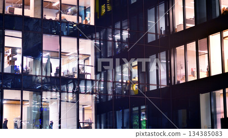 Modern office building in city center illuminated at night. Rows of lit windows against the architectural grid of a modern facade. Concrete and glass facade in its night version. Modern office building in city center illuminated at night. Rows of lit windows against the architectural grid of a modern facade. Concrete and glass facade in its night version. 134385083
