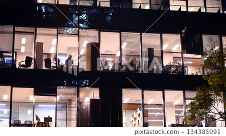 Modern office building in city center illuminated at night. Rows of lit windows against the architectural grid of a modern facade. Concrete and glass facade in its night version. Modern office building in city center illuminated at night. Rows of lit windows against the architectural grid of a modern facade. Concrete and glass facade in its night version. 134385091