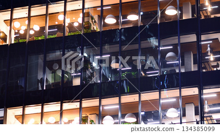 Modern office building in city center illuminated at night. Rows of lit windows against the architectural grid of a modern facade. Concrete and glass facade in its night version. Modern office building in city center illuminated at night. Rows of lit windows against the architectural grid of a modern facade. Concrete and glass facade in its night version. 134385099