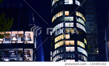 Modern office building in city center illuminated at night. Rows of lit windows against the architectural grid of a modern facade. Concrete and glass facade in its night version. Modern office building in city center illuminated at night. Rows of lit windows against the architectural grid of a modern facade. Concrete and glass facade in its night version. 134385102