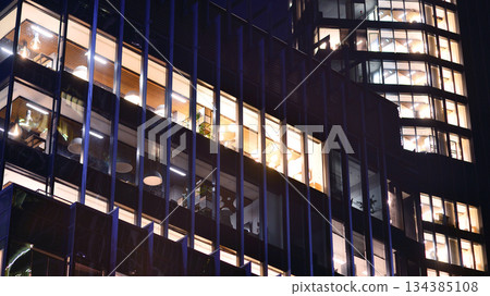 Modern office building in city center illuminated at night. Rows of lit windows against the architectural grid of a modern facade. Concrete and glass facade in its night version. Modern office building in city center illuminated at night. Rows of lit windows against the architectural grid of a modern facade. Concrete and glass facade in its night version. 134385108