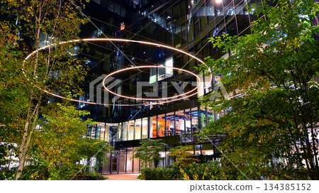 Modern office building in city center illuminated at night. Rows of lit windows against the architectural grid of a modern facade. Concrete and glass facade in its night version. 134385152