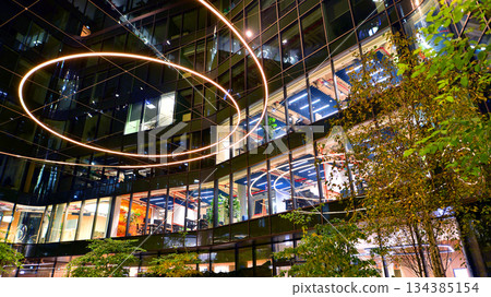 Modern office building in city center illuminated at night. Rows of lit windows against the architectural grid of a modern facade. Concrete and glass facade in its night version. 134385154