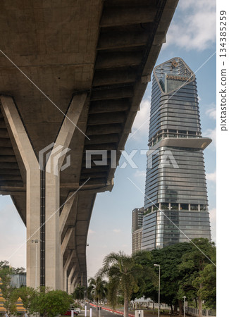 A tall, modern skyscraper rises beside a massive concrete elevated highway structure 134385259
