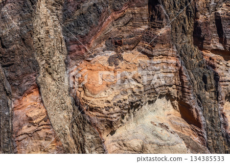 Eroded volcanic cliff layers in Sao Lourenco Madeira reveal red ochre and black tones 134385533