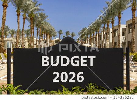 Budget 2026 symbol. Concept words Budget 2026 on beautiful black road sign. Beautiful palm trees palm-trees and blue sky background. Business and budget 2026 concept. Copy space. 134386253