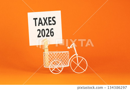 Taxes 2026 symbol. Concept words Taxes 2026 on beautiful white paper on wooden clothespin. Beautiful orange background. Beautiful miniature bicycle. Business taxes 2026 new year concept. Copy space. 134386297