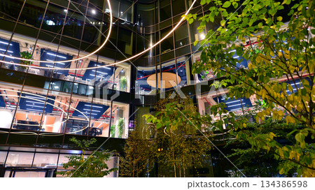 Modern office building in city center illuminated at night. Rows of lit windows against the architectural grid of a modern facade. Concrete and glass facade in its night version. Modern office building in city center illuminated at night. Rows of lit windows against the architectural grid of a modern facade. Concrete and glass facade in its night version. 134386598