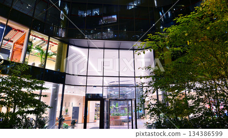 Modern office building in city center illuminated at night. Rows of lit windows against the architectural grid of a modern facade. Concrete and glass facade in its night version. Modern office building in city center illuminated at night. Rows of lit windows against the architectural grid of a modern facade. Concrete and glass facade in its night version. 134386599