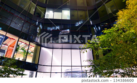 Modern office building in city center illuminated at night. Rows of lit windows against the architectural grid of a modern facade. Concrete and glass facade in its night version. Modern office building in city center illuminated at night. Rows of lit windows against the architectural grid of a modern facade. Concrete and glass facade in its night version. 134386600