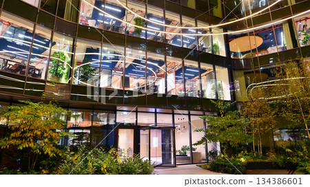 Modern office building in city center illuminated at night. Rows of lit windows against the architectural grid of a modern facade. Concrete and glass facade in its night version. 134386601