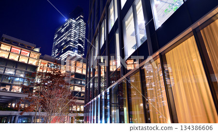Modern office building in city center illuminated at night. Rows of lit windows against the architectural grid of a modern facade. Concrete and glass facade in its night version. 134386606