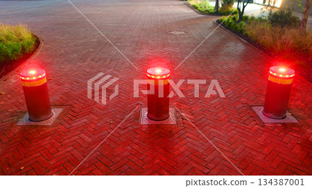 Automatic security hydraulic bollards in night. Lifting metallic bollards to enable or block traffic to protect property. Automatic security hydraulic bollards in night. Lifting metallic bollards to enable or block traffic to protect property. 134387001