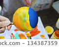 Women's hands carefully paint a brightly colored Christmas ball 134387359