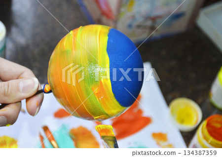 Women's hands carefully paint a brightly colored Christmas ball 134387359