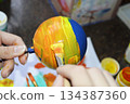 Women's hands carefully paint a brightly colored Christmas ball 134387360