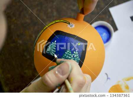 Female hands carefully painting a Christmas ball in vibrant orange hues 134387361