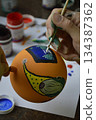 Female hands carefully painting a Christmas ball in vibrant orange hues 134387362
