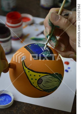 Female hands carefully painting a Christmas ball in vibrant orange hues 134387362