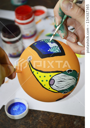 Female hands carefully painting a Christmas ball in vibrant orange hues 134387365