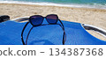 A pair of dark-framed sunglasses rests on a blue beach chair by the sea 134387368