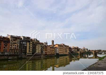 Florence, Arno River scenery: cityscape reflected on the water and Ponte Vecchio in the distance Florence, Arno River scenery: cityscape reflected on the water and Ponte Vecchio in the distance 134387375