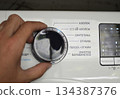 A hand turning the wheel of a washing machine - program labels 134387376