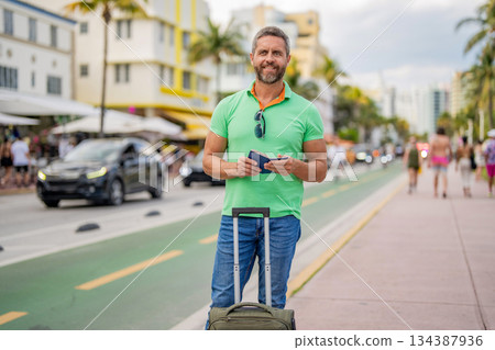 Man 40s traveler. Tourist on summer vacation. Traveler luggage for summer trip. Summer tour. Traveler enjoy summer trip. Hispanic tourist traveler on city street. Tourist with suitcase and passport Man 40s traveler. Tourist on summer vacation. Traveler luggage for summer trip. Summer tour. Traveler enjoy summer trip. Hispanic tourist traveler on city street. Tourist with suitcase and passport 134387936