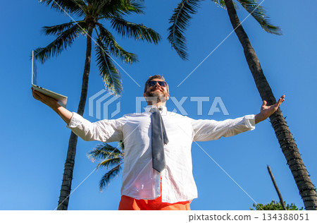 Businessman on summer vacation. Online freelance work. Businessman boss with laptop. Business man using laptop near palm tree. Business trip. Man freelance work online at beach. Happy holiday 134388051