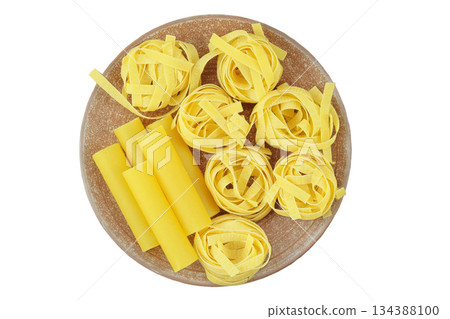 Various of uncooked pasta. Fettuccine, tagliatelle and cannelloni on ceramic plate isolated on white background. Top view. Various of uncooked pasta. Fettuccine, tagliatelle and cannelloni on ceramic plate isolated on white background. Top view. 134388100