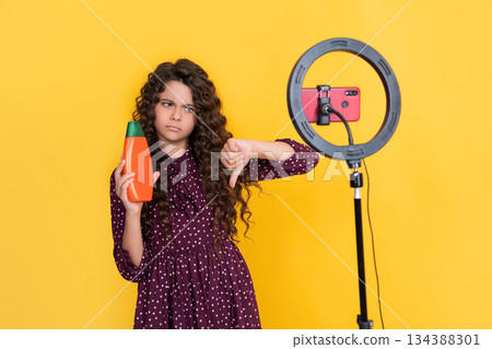 kid with long curly hair making video for blog hold shampoo. thumb down 134388301