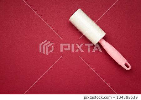 Cloth fabrics cleaner lint roller brush with paper roll on red background. Sticky roller, pet cat dog fur dust hair remover Cloth fabrics cleaner lint roller brush with paper roll on red background. Sticky roller, pet cat dog fur dust hair remover 134388539