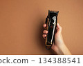 Hair clipper in hand on brown background. Modern hair clipper. Space for text 134388541