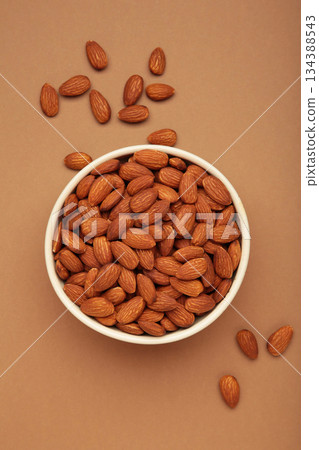 Almonds in bowl on brown background. Whole and dried nuts. Vertical photo Almonds in bowl on brown background. Whole and dried nuts. Vertical photo 134388543