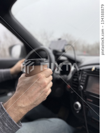 Driver holding coffee cup inside car during commute with blurred background 134388879