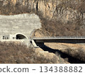 Mountain tunnel with adjoining bridge in rural landscape, featuring rocky cliffs and dry vegetation Mountain tunnel with adjoining bridge in rural landscape, featuring rocky cliffs and dry vegetation 134388882