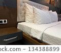 Comfortable bed with white pillows and wooden nightstand in modern hotel room interior background Comfortable bed with white pillows and wooden nightstand in modern hotel room interior background 134388899