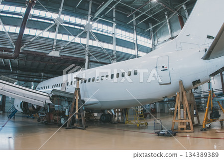 White passenger jetliner in the aviation hangar. Aircraft under maintenance. Checking mechanical systems for flight operations 134389389